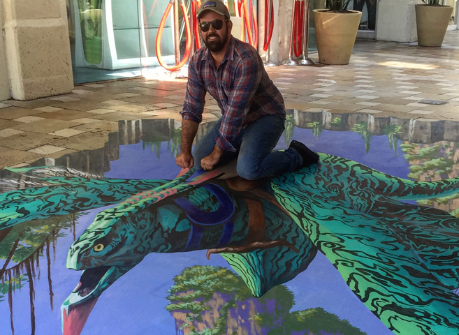 A person crouches beside a colourful pavement painting that appears to open into a deep landscape.