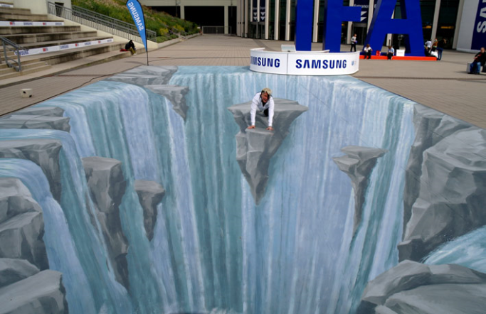 A pavement painting of a waterfall and deep chasm, with a person positioned inside its apparent space.